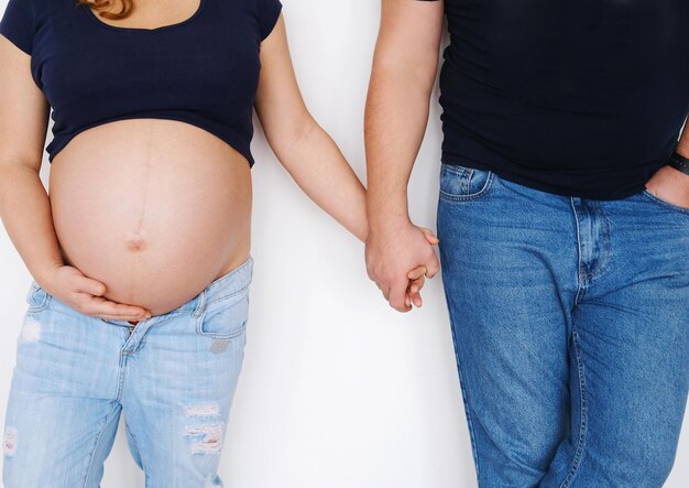 Una pareja, un hombre y una mujer embarazada, se paran cerca de una pared blanca y se toman de la mano El concepto de apoyo y amor en la familia