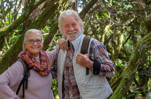 Pareja de hombre y mujer mayores disfrutando de una caminata de montaña en el bosque entre troncos y ramas cubiertas de musgo durante la temporada de otoño - concepto de diversión y jubilados activos