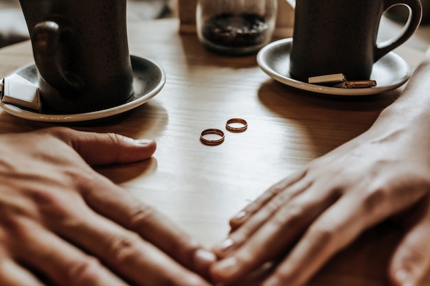 Pareja de hombre y mujer de recién casados se dan la mano con anillos en un café con una taza de café. Los novios están enamorados