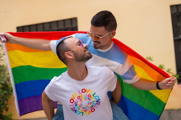 Foto pareja de hombres homosexuales montando en la parte superior de la espalda besándose en la fiesta del orgullo con el concepto lgbt de la bandera del arco iris