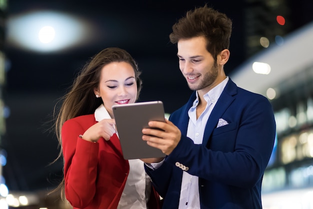 Pareja de hombres de negocios que usan una tableta al aire libre en la noche en un entorno de ciudad moderna