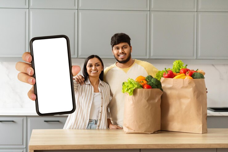 Foto una pareja india amorosa muestra bolsas llenas de comestibles y teléfonos inteligentes