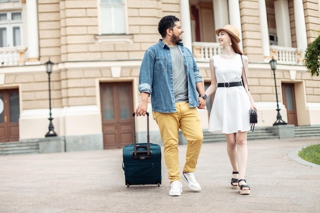 Pareja internacional de turistas caminando por una calle europea con equipaje de viaje