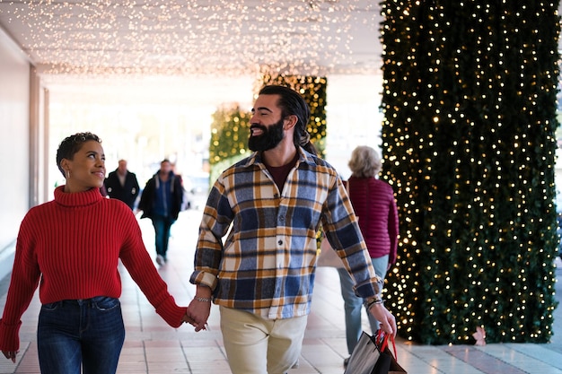 Pareja interracial saliendo a hacer compras navideñas en la zona comercial