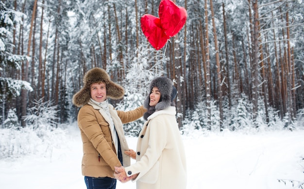 Foto pareja de invierno enamorada. niño y niña abrazándose en el invierno la nieve y el bosque de hadas con globos.