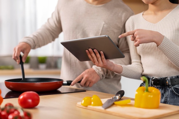 Foto pareja irreconocible usando tableta digital mientras cocina en casa