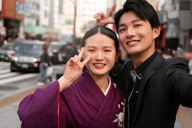 Foto pareja japonesa celebra el día de la mayoría de edad al aire libre tomándose una selfie