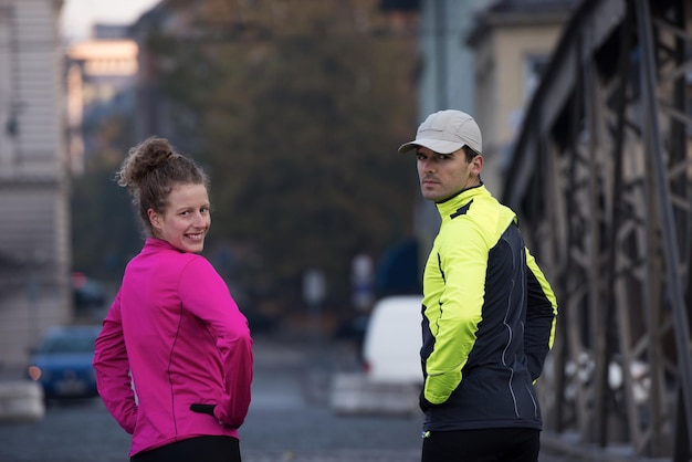 pareja de jogging calentándose y estirándose antes de correr por la mañana en la ciudad