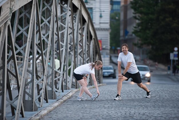 pareja de jogging calentándose y estirándose antes de la mañana haciendo ejercicio de entrenamiento en la ciudad con el amanecer en el fondo