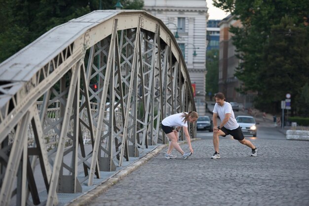 pareja de jogging calentándose y estirándose antes de la mañana haciendo ejercicio de entrenamiento en la ciudad con el amanecer en el fondo