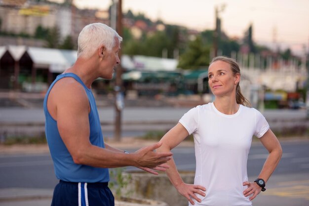 pareja de jogging calentándose y estirándose antes de la mañana haciendo ejercicio de entrenamiento en la ciudad con el amanecer en el fondo