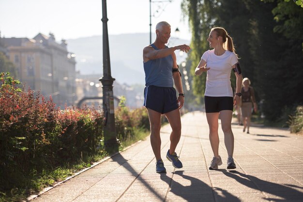 la pareja de jogging revisa la lista de reproducción de música en el teléfono y planifica la ruta antes de hacer ejercicio por la mañana con el amanecer en la ciudad y el sol en el fondo