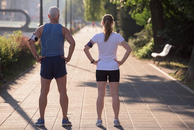 la pareja de jogging revisa la lista de reproducción de música en el teléfono y planifica la ruta antes de hacer ejercicio por la mañana con el amanecer en la ciudad y el sol en el fondo