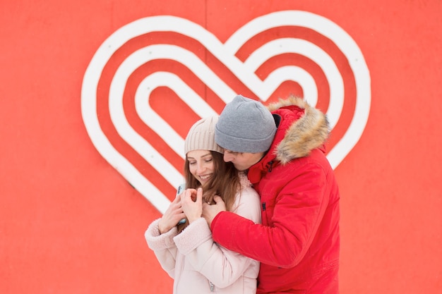 Pareja joven abrazándose en la ciudad cerca de gran corazón en la pared. Día de San Valentín