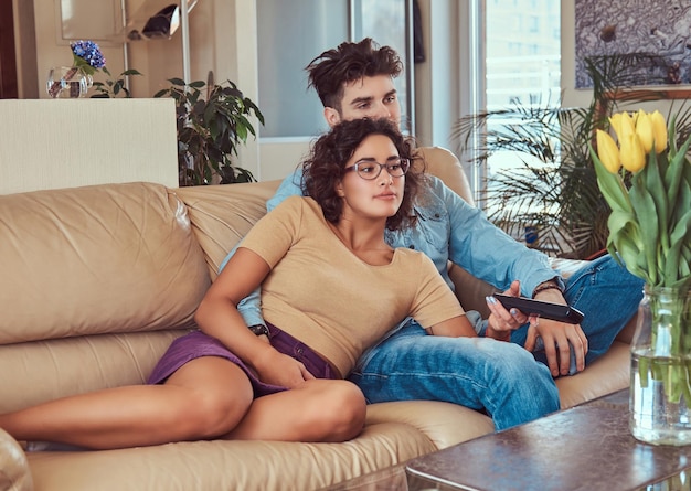 Pareja joven abrazándose mientras ve la televisión en su sala de estar.