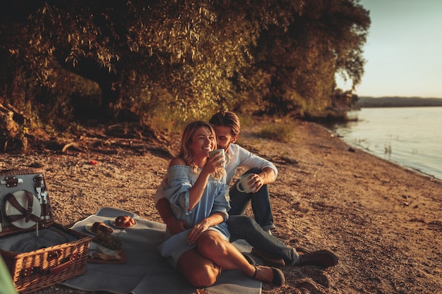 pareja joven, se abrazar, en, comida campestre, y, bebida, café, en, ocaso