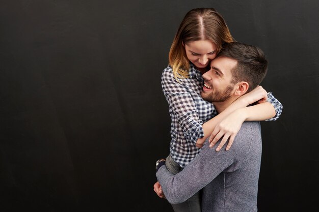 Pareja joven, abrazar, y, sonriente, contra, de, fondo negro