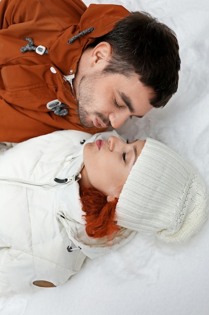 Una pareja joven acostada y besándose en la nieve al aire libre en invierno de cerca