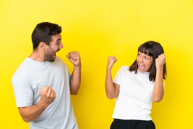 Pareja joven aislada de fondo amarillo celebrando una victoria en posición de ganador