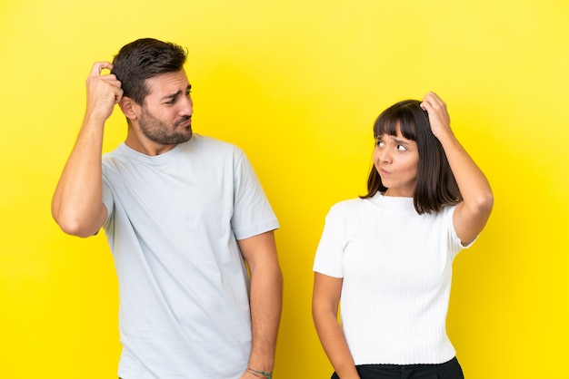 Foto una pareja joven aislada de fondo amarillo que tiene dudas mientras se rasca la cabeza