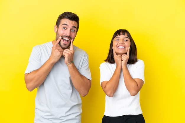 Una pareja joven aislada de fondo amarillo sonriendo con una expresión feliz y agradable