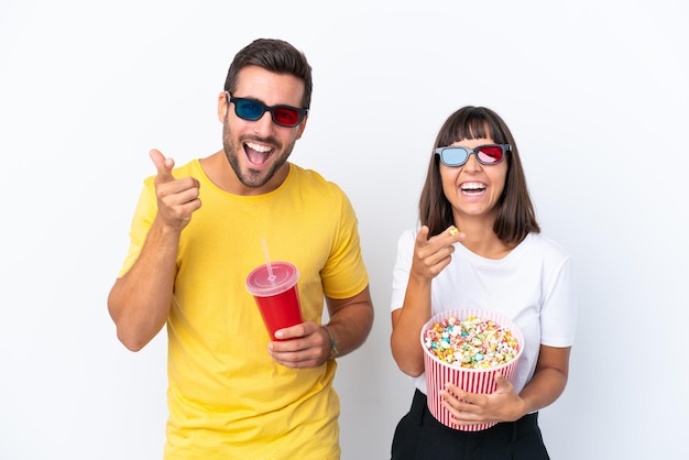 Una pareja joven aislada de fondo blanco con gafas 3d y sosteniendo un gran cubo de palomitas de maíz mientras apunta al frente