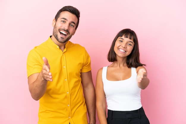 Una pareja joven aislada de fondo rosa dándose la mano para cerrar un buen trato