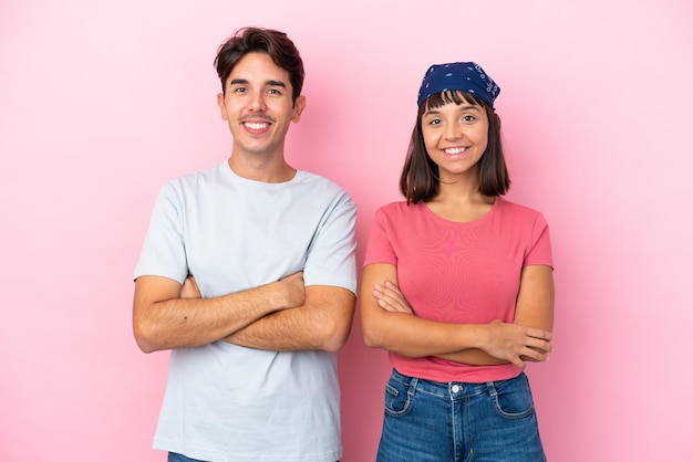 Pareja joven aislada sobre fondo rosa manteniendo los brazos cruzados en posición frontal