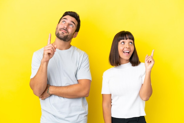 Pareja joven aislado sobre fondo amarillo apuntando una gran idea y mirando hacia arriba