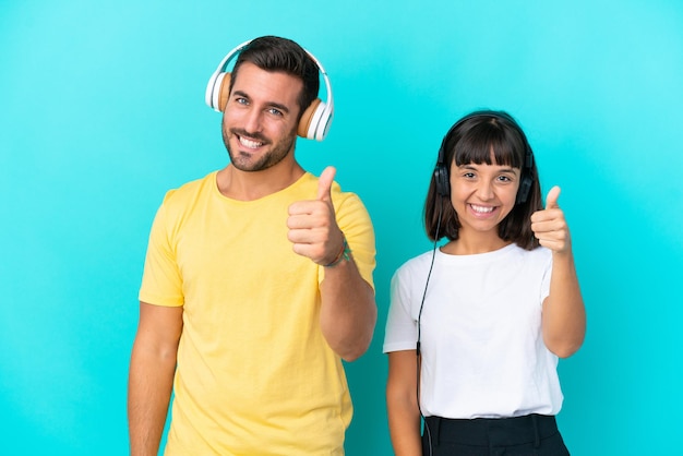 Pareja joven aislado sobre fondo azul escuchando música y con el pulgar hacia arriba