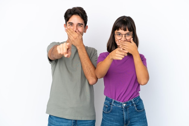 Pareja joven aislado sobre fondo blanco aislado apuntando con el dedo a alguien y riendo