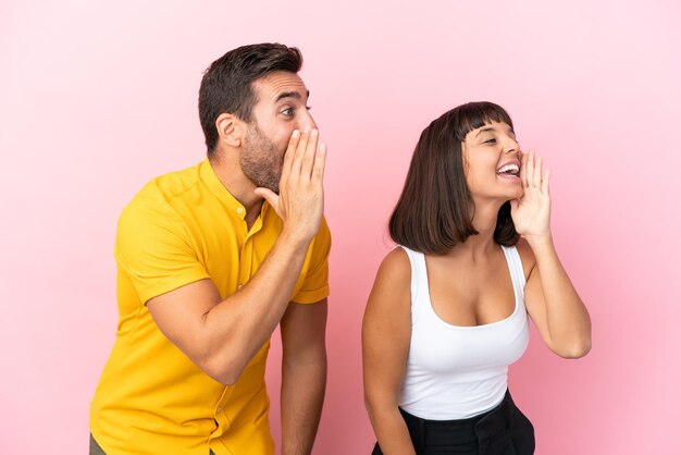 Foto pareja joven aislado sobre fondo rosa gritando con la boca abierta hacia el lateral