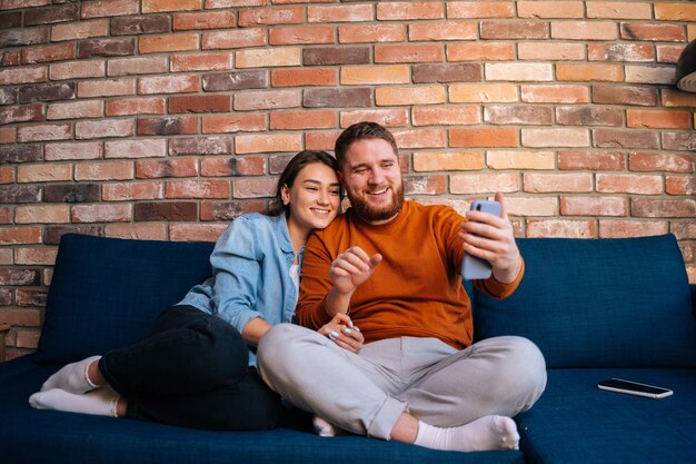 Pareja joven alegre agitando las manos y saludando en una videollamada de teléfono móvil en línea sentados juntos