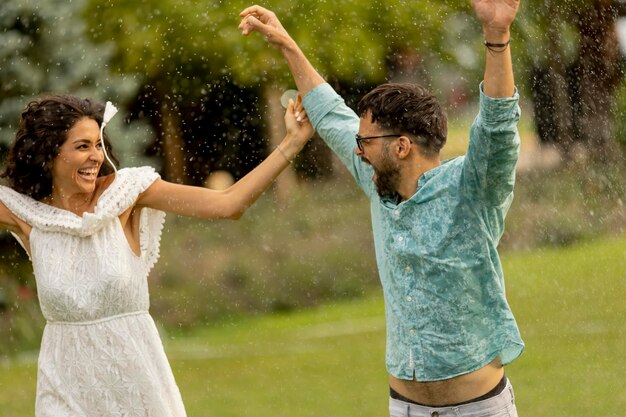 Una pareja joven y alegre atrapada por la lluvia de verano en el parque