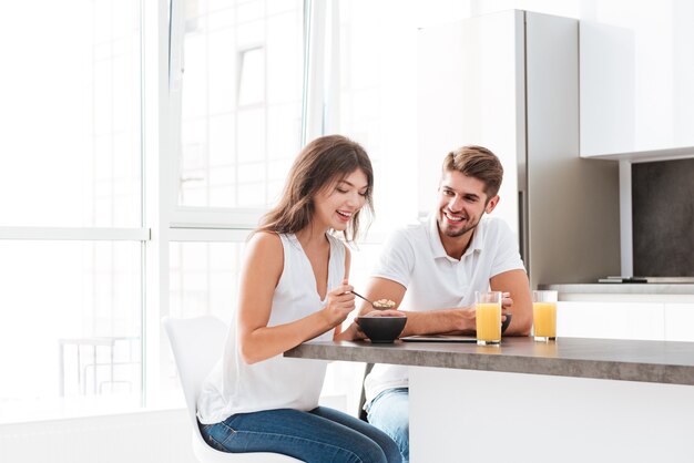 Foto pareja joven alegre desayunando en la cocina de casa