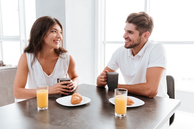 Pareja joven alegre sentado y tomando café en la mesa de la cocina