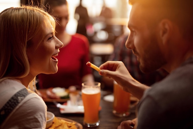 Pareja joven almorzando con amigos en un restaurante El joven está alimentando a su novia con papas fritas