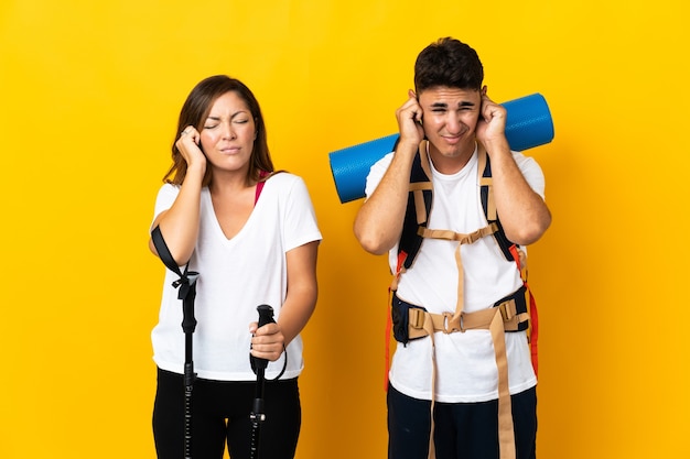 Pareja joven alpinista con una gran mochila en amarillo frustrado y cubriendo las orejas