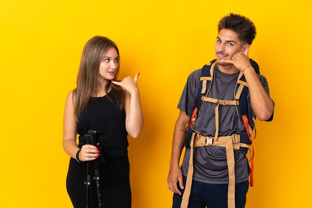 Pareja joven alpinista con una gran mochila en amarillo haciendo gesto de teléfono. Llámame señal