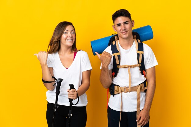 Pareja joven alpinista con una mochila grande en amarillo apuntando hacia el lado para presentar un producto