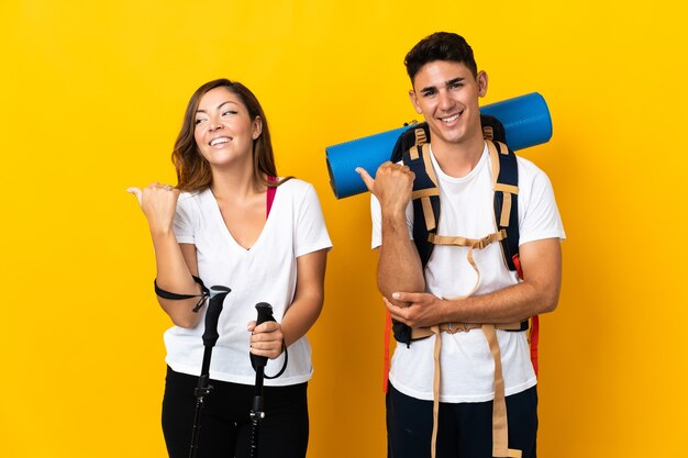 Pareja joven alpinista con una mochila grande en amarillo apuntando hacia el lado para presentar un producto