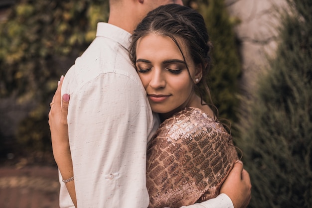 Pareja joven de amantes hombre y mujer en ropa de moda festiva se abrazan. Peinado casual ligero para mujeres con permanente. Naturaleza de verano fuera de fondo.