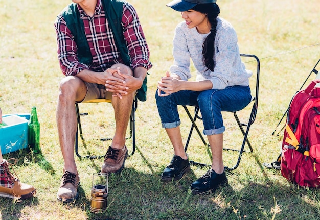 Una pareja joven y un amigo sentados en una silla discuten juntos acampar en verano, enfocan la pierna