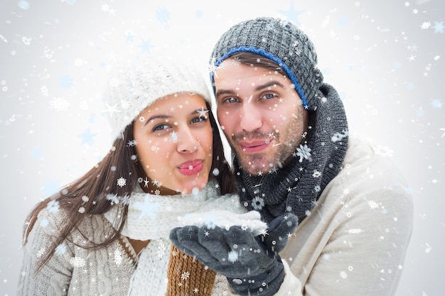 Pareja joven atractiva en ropa de abrigo que sopla contra la nieve que cae