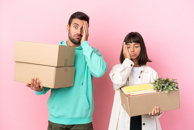 Pareja joven belleza moviéndose en casa nueva entre cajas aisladas sobre fondo rosa con sorpresa y expresión facial conmocionada