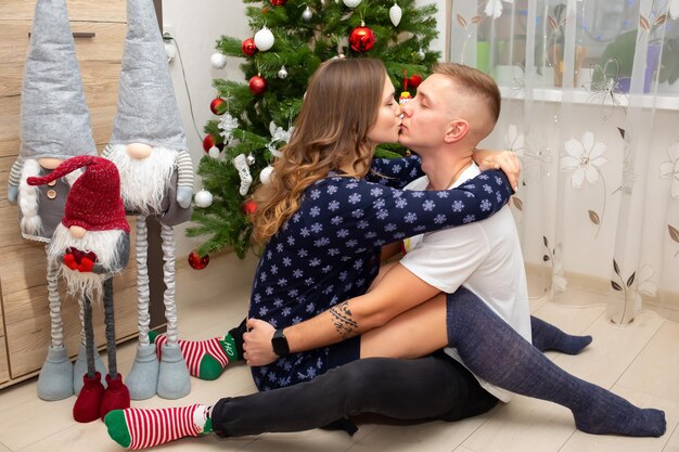 Una pareja joven se besa cerca del árbol de Navidad y dará regalos.