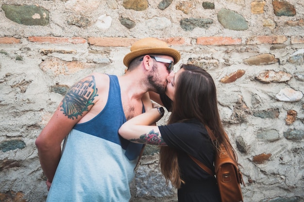 Una pareja joven besándose contra una pared de piedra.