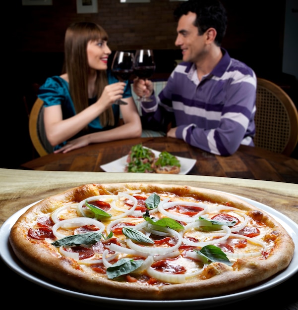 Pareja joven brindando vino tinto en la pizzería