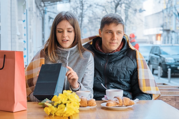 Pareja joven en café al aire libre con bolsas de compras