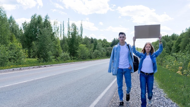 Una pareja joven camina por el lado de la carretera con una caja de cartón en sus manos con un lugar para t